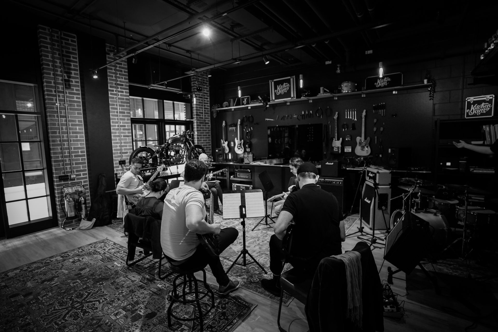 Musicians rehearsing in a dimly lit recording studio with microphones, instruments, and equipment scattered around.