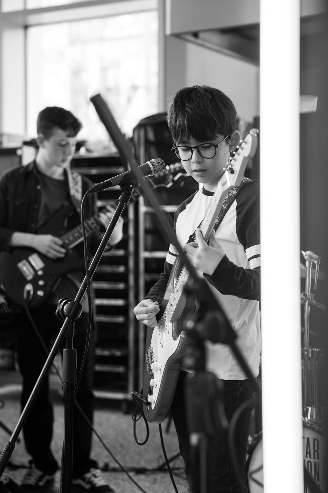 A black and white photo of a boy playing a guitar in front of a microphone.