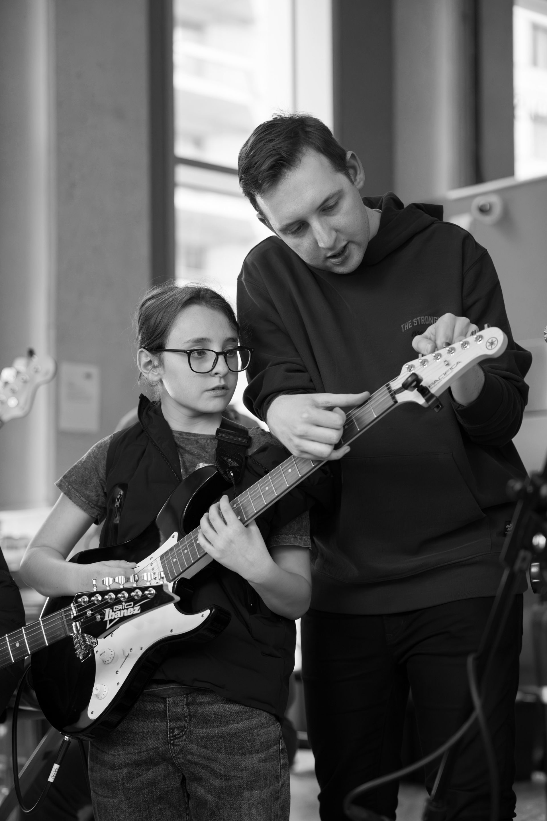 A man is teaching a young boy how to play an electric guitar.
