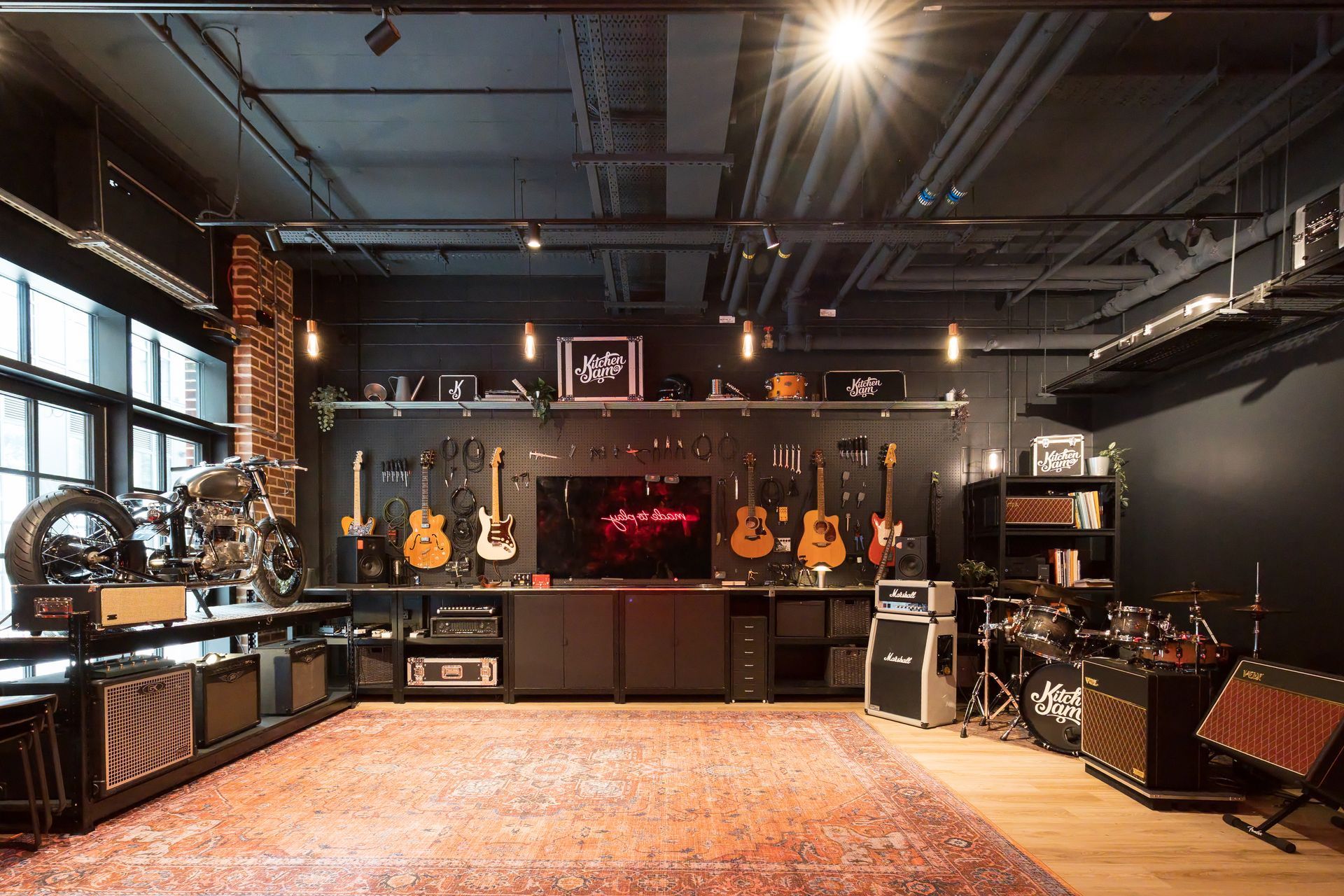 KitchenJam Canary Wharf studio with guitars, amplifiers, drums, and a patterned rug under warm ceiling lights