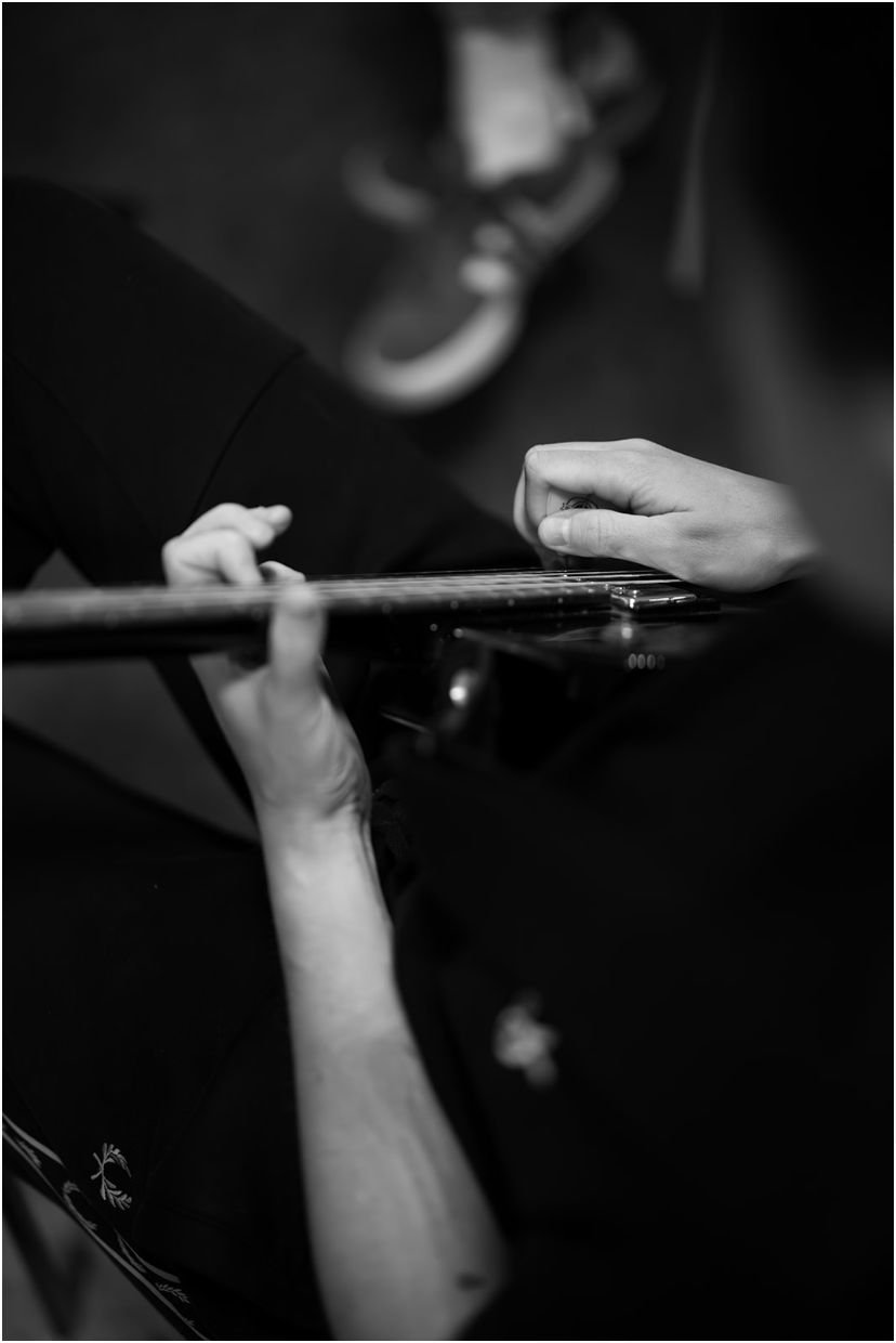 Black and white photo of hands playing a guitar; close-up, indoors.