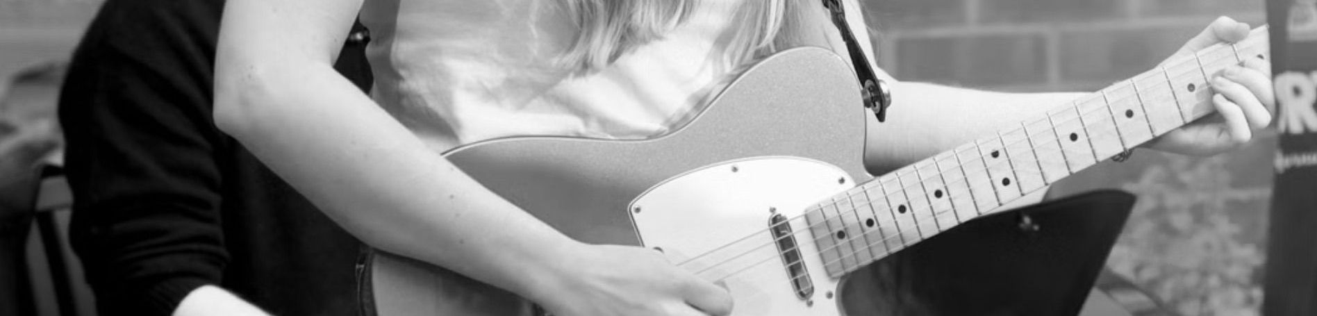 A person playing an electric guitar, close up view of the instrument and the hands of the guitarist.