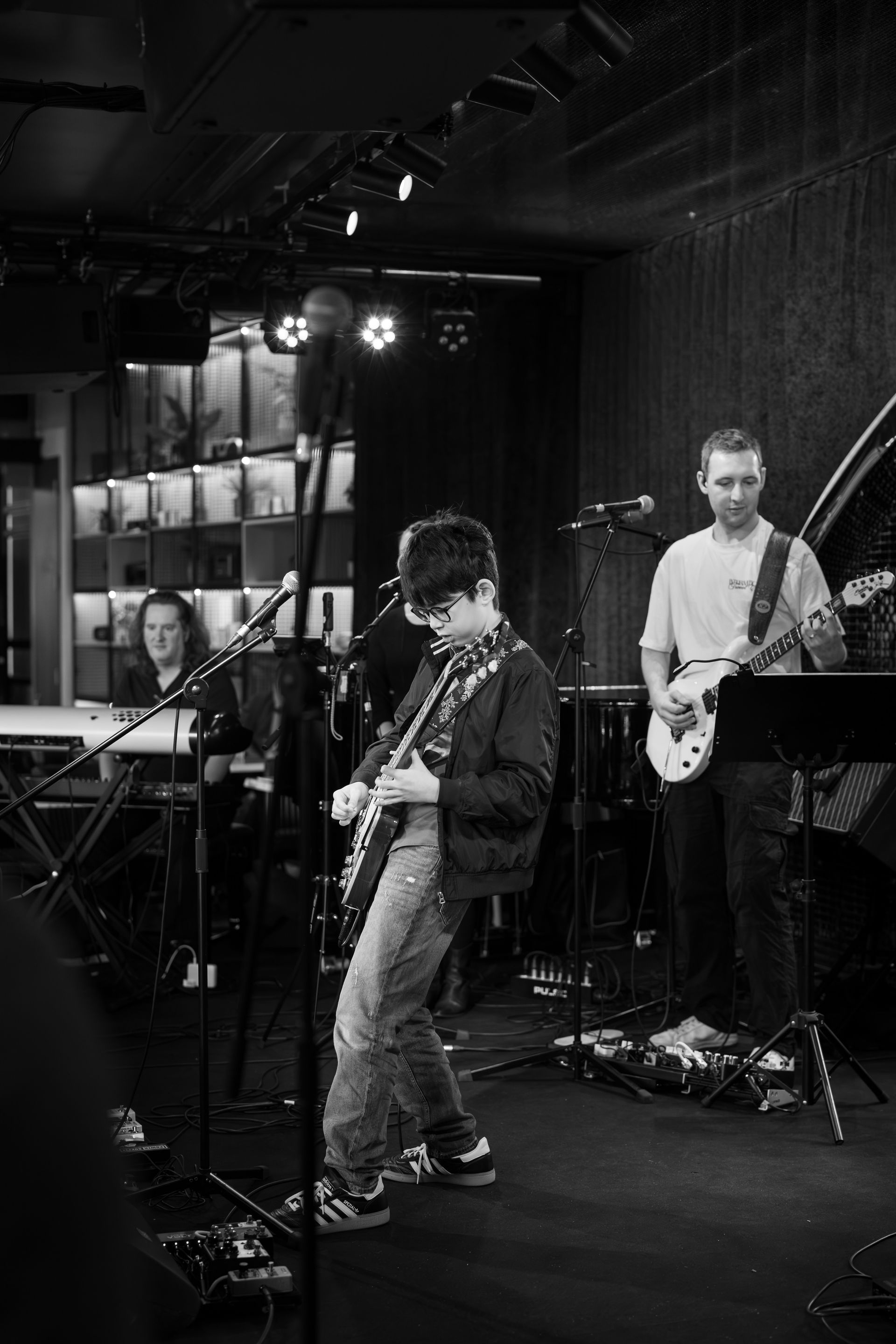 Musician on stage playing guitar. A person in the foreground taking a photo. Stage has a purple curtain backdrop.