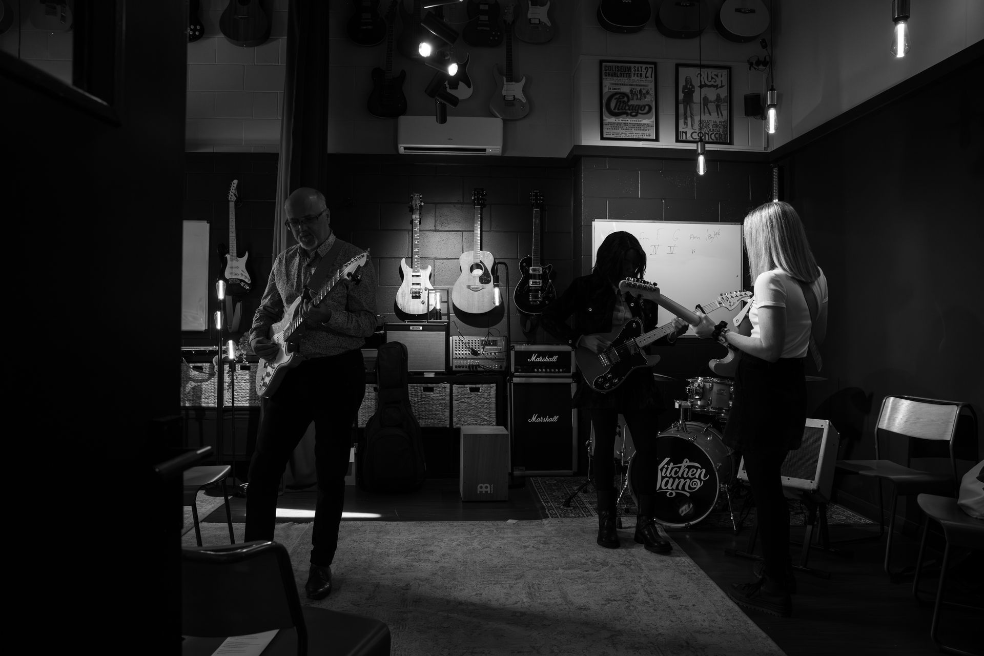 Band playing guitars in a music store, guitars on the wall, stage, amplifiers, chairs.