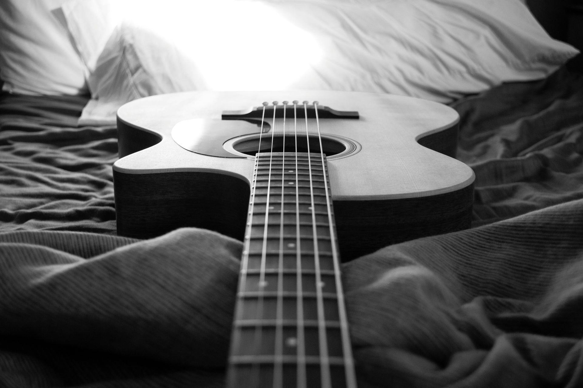 Acoustic guitar resting on a wrinkled blanket with a soft light in the background.