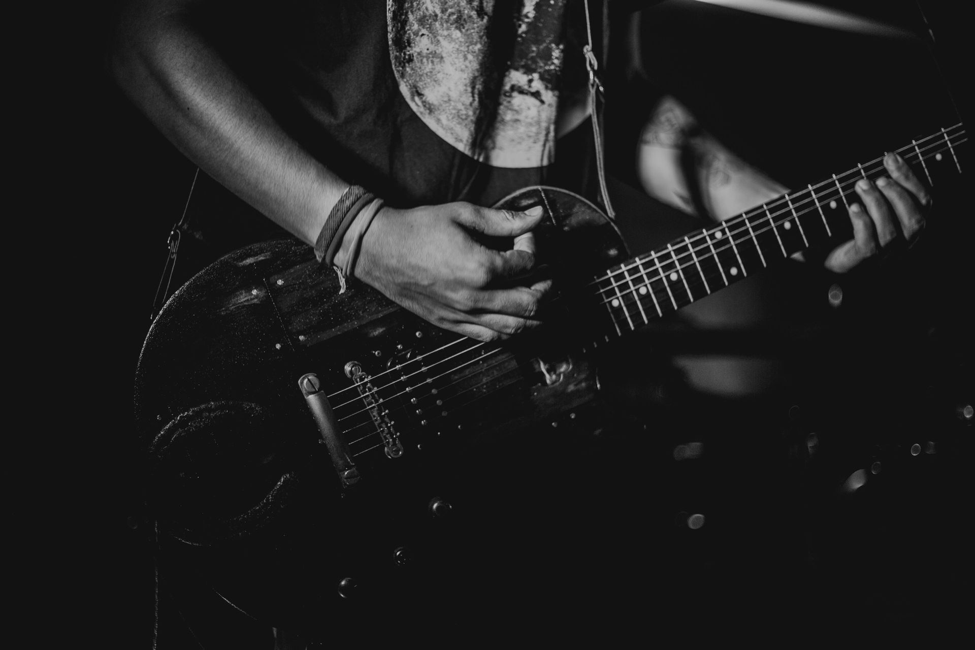 Person playing a black electric guitar in dim lighting, hands strumming and fretting.