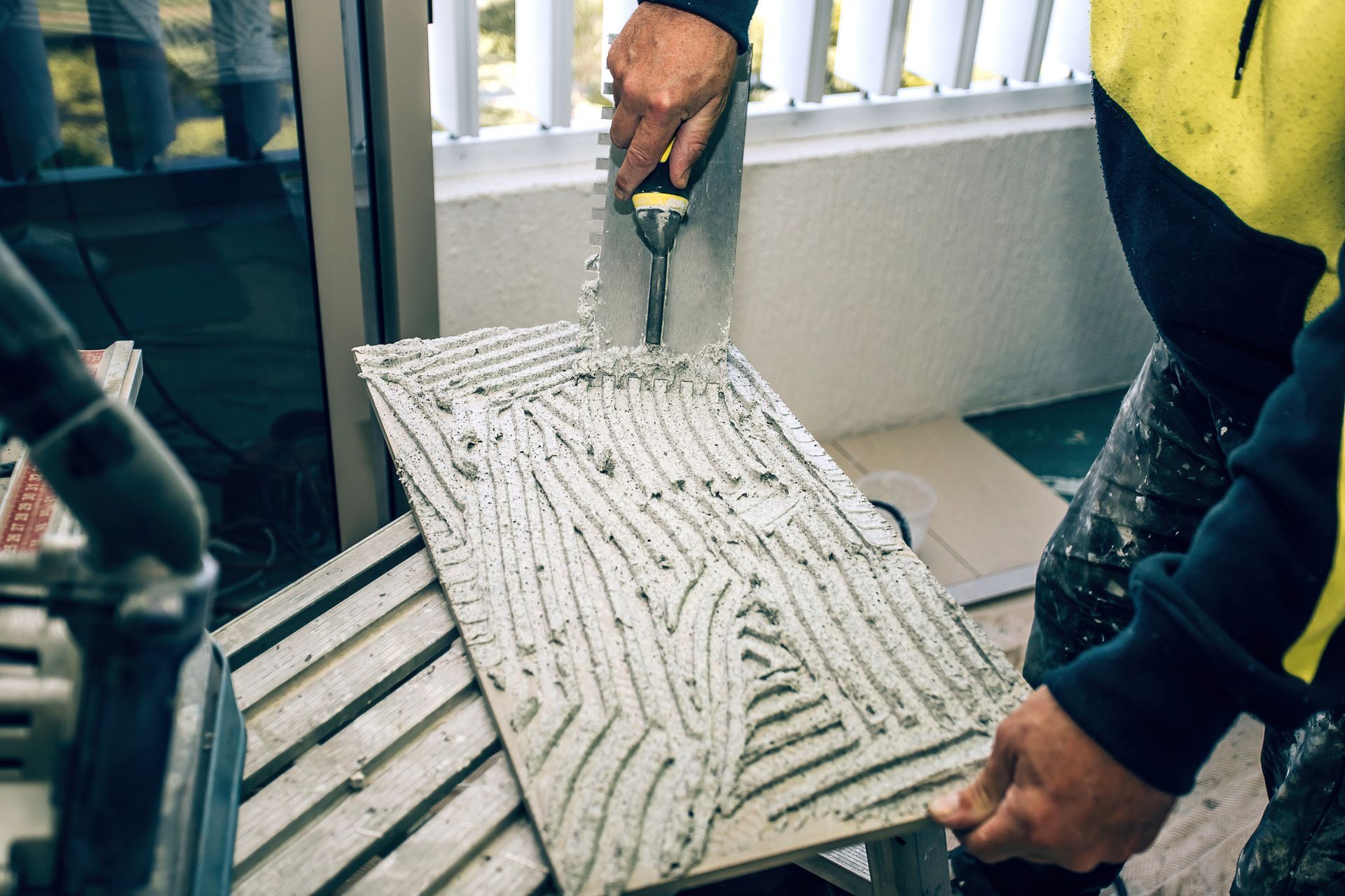 A man is applying adhesive to a tile with a trowel.