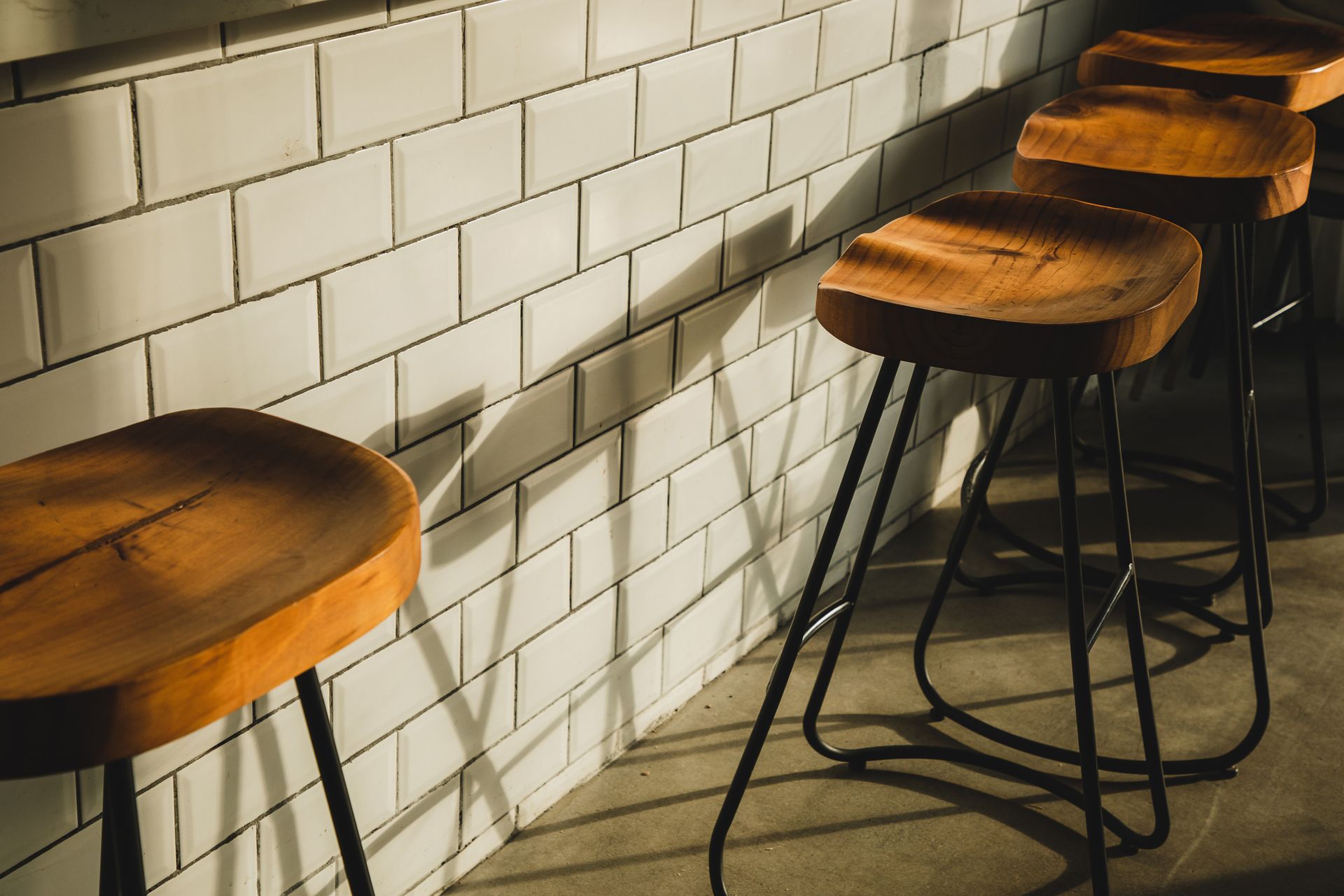 A row of wooden bar stools in front of a white brick wall.