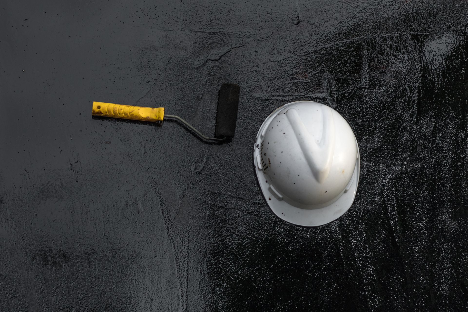 A hard hat and a roller are on a black surface.