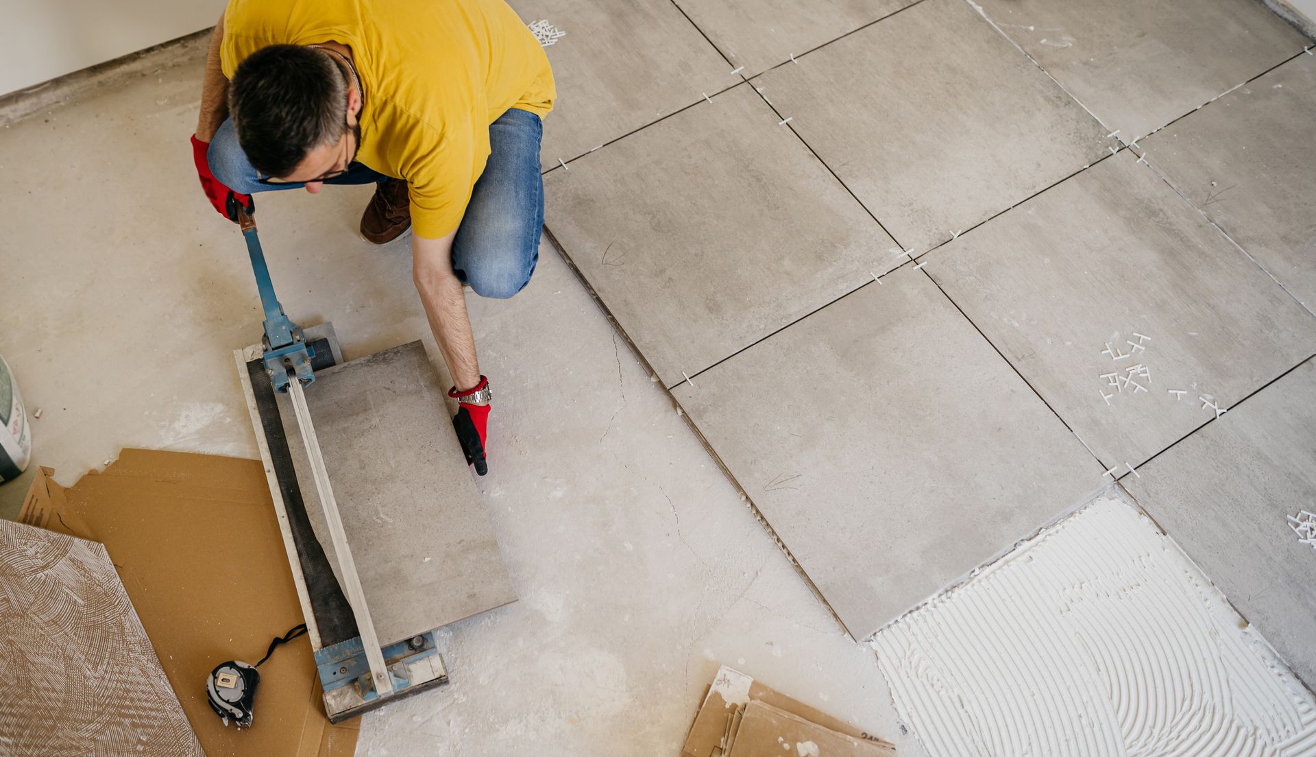 A man is installing tiles on a floor with a tile cutter.