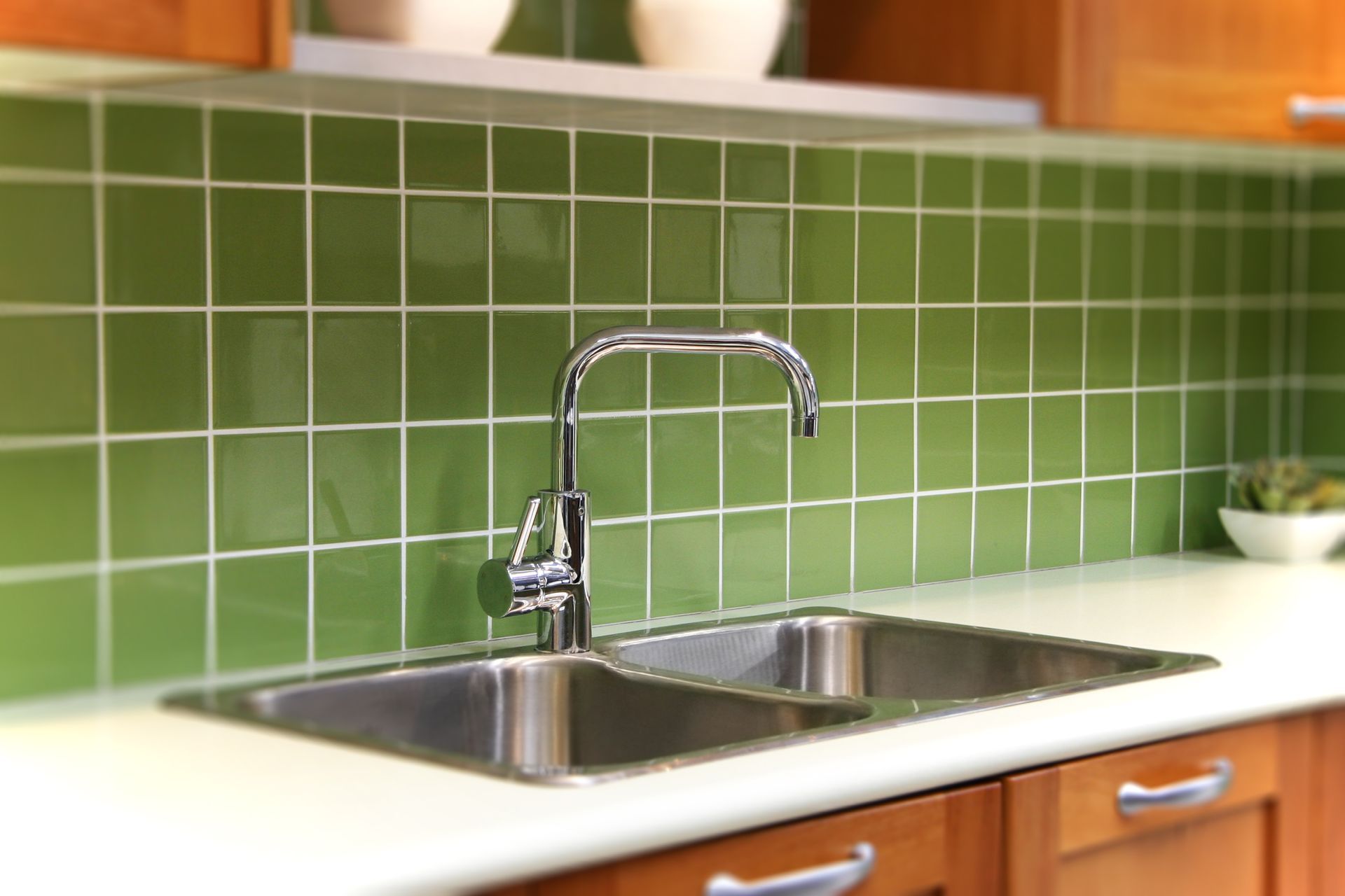 A kitchen with two sinks and green tiles on the wall
