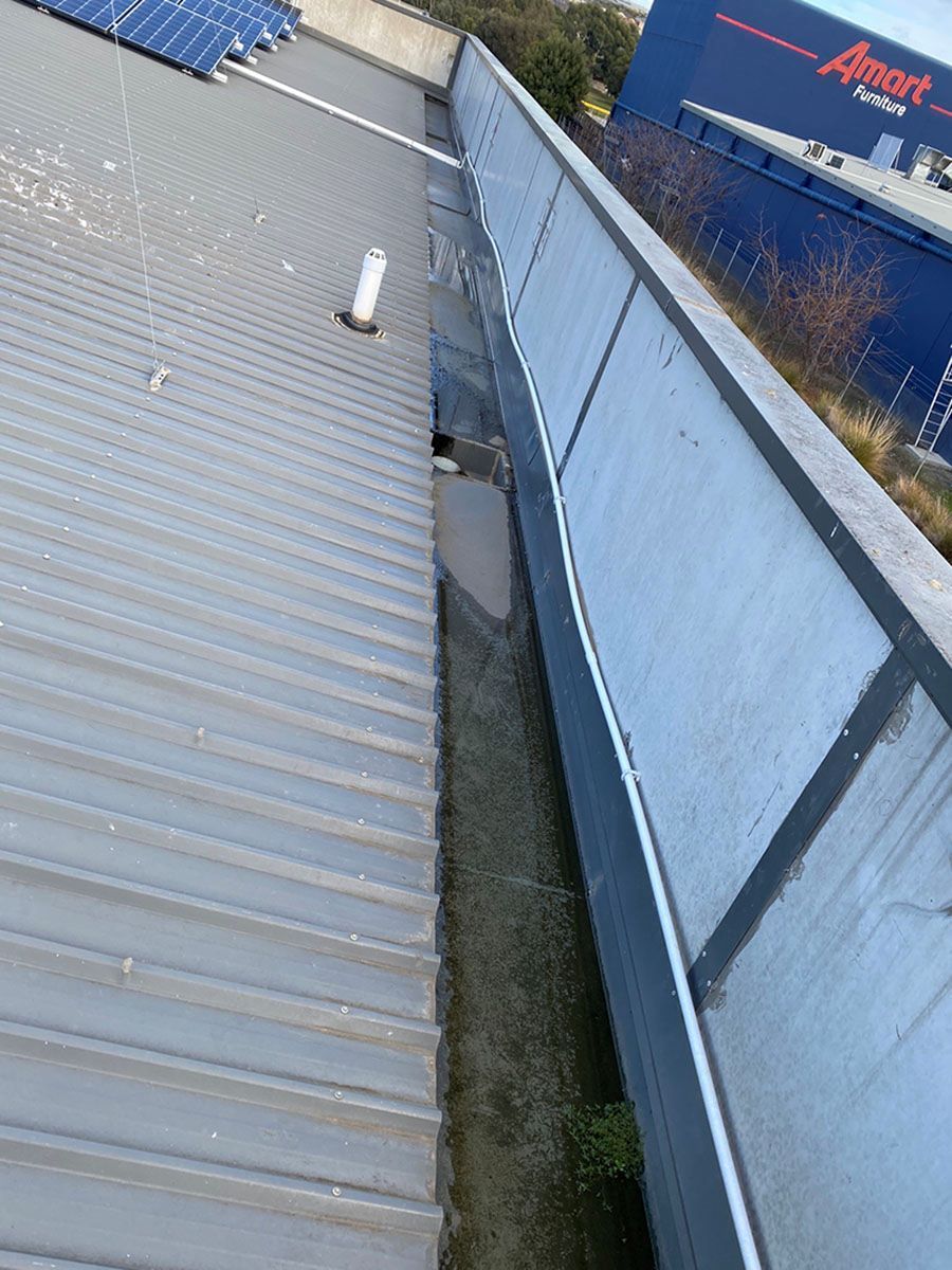 A Gutter on the Side of a Building With a Blue Building in the Background — Fig Facility Services in Lara, VIC
