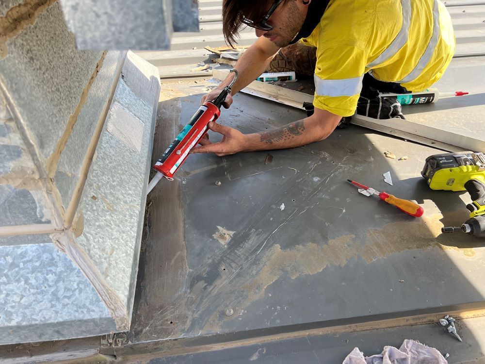 Person Applying Sealant on Rooftop Edge, Wearing a Yellow and Black Outfit — Fig Facility Services in Lara, VIC