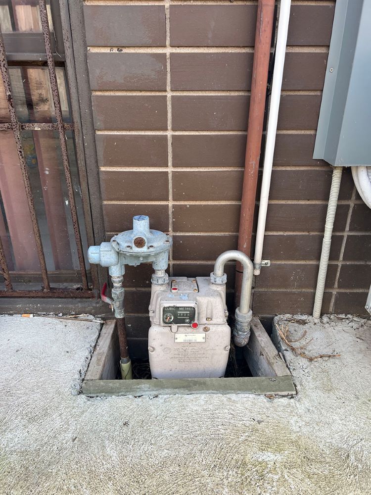 A Gas Meter is Sitting in a Hole in the Ground Next to a Brick Wall — Fig Facility Services in Lara, VIC