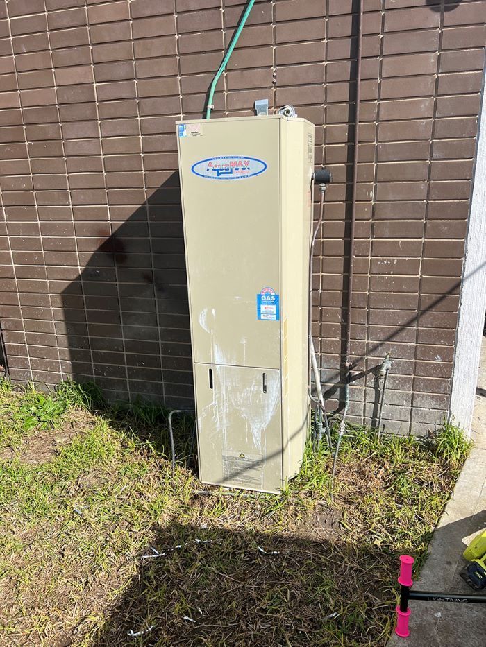 A Water Heater is Sitting in the Grass Next to a Brick Wall — Fig Facility Services in Lara, VIC