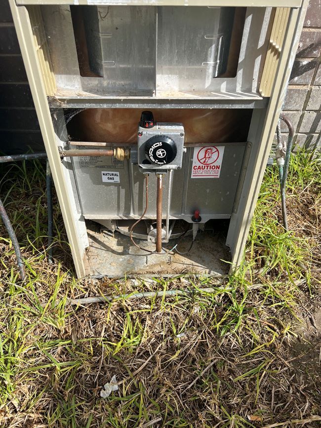 A Water Heater is Sitting in the Grass Next to a Brick Building — Fig Facility Services in Lara, VIC