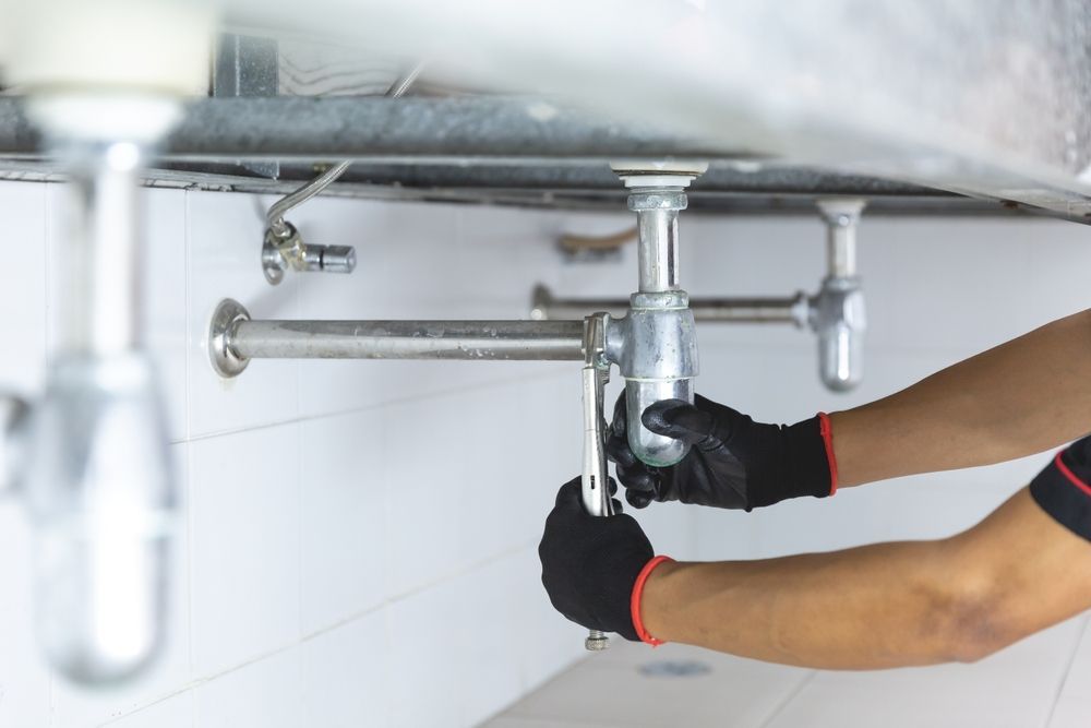 A Plumber is Fixing a Sink Pipe With a Wrench — Fig Facility Services in Lara, VIC