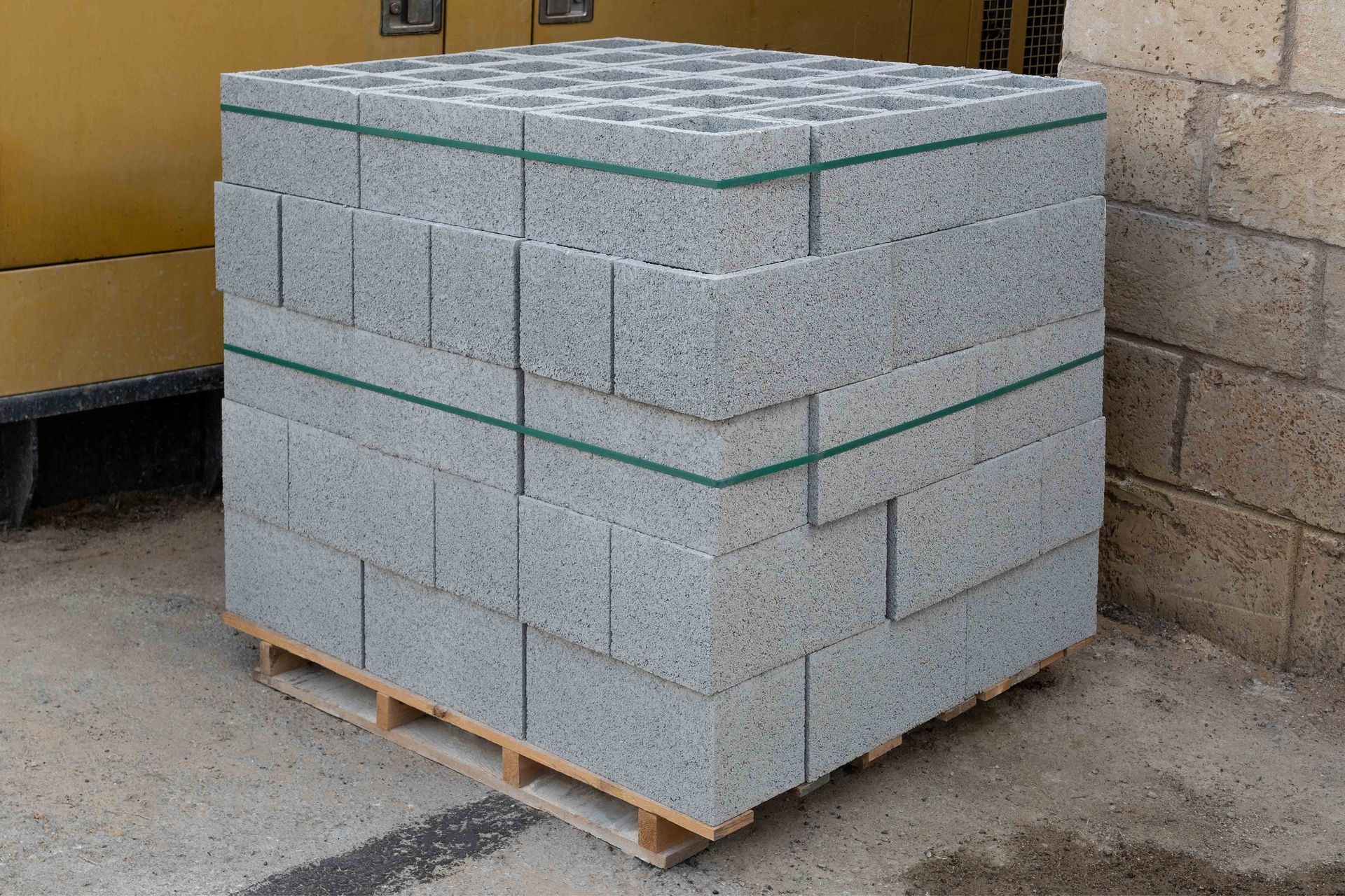 Pallet of gray cinder blocks bound with green straps.