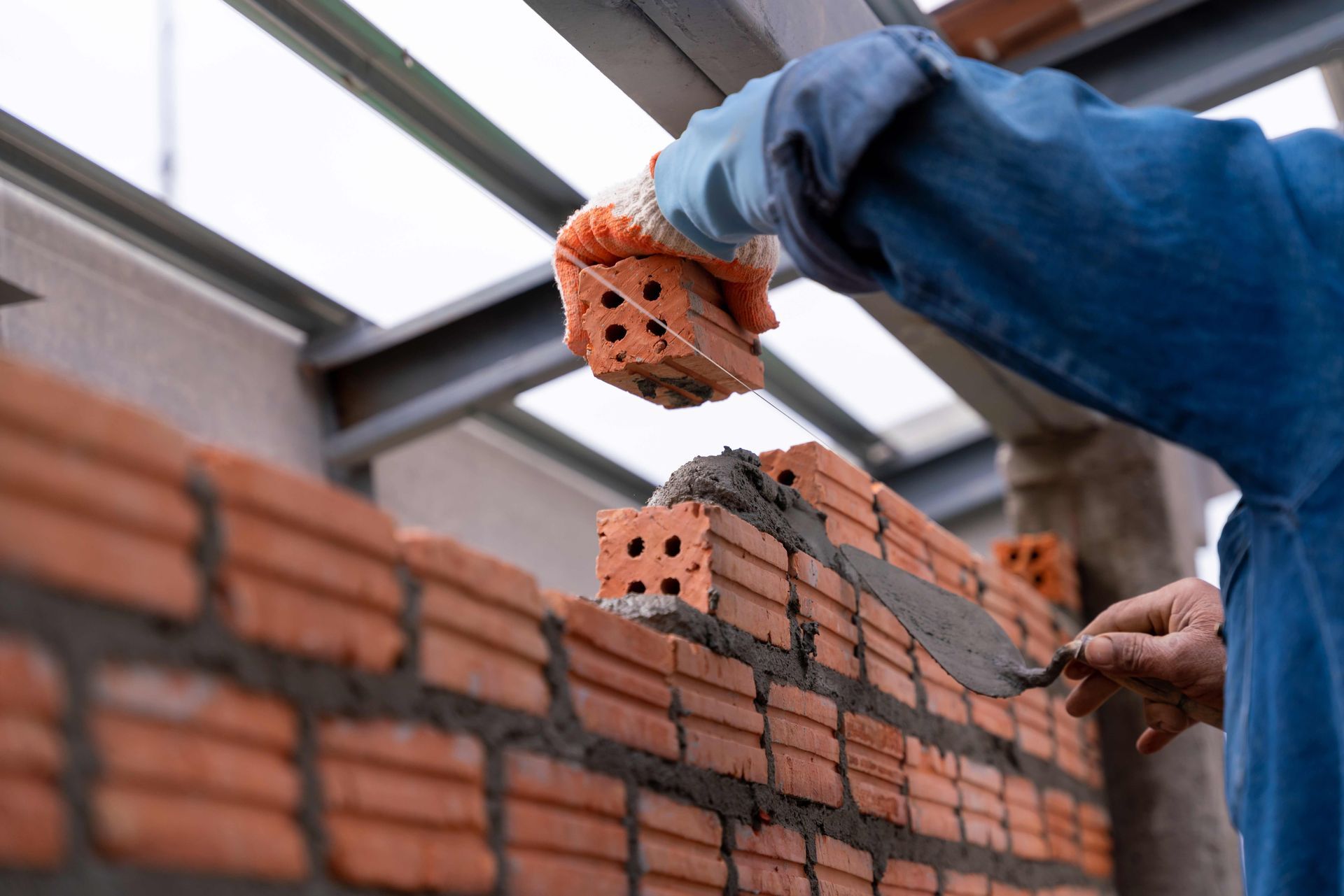 Bricklayer laying bricks on a wall, wearing gloves.