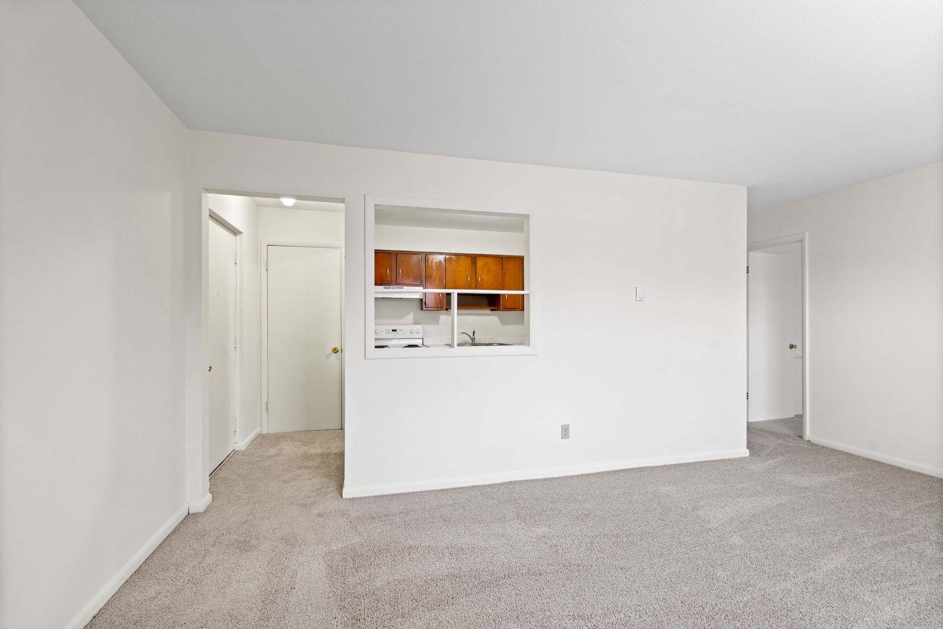 Photo of a living room area with the kitchen and front entrance in the background
