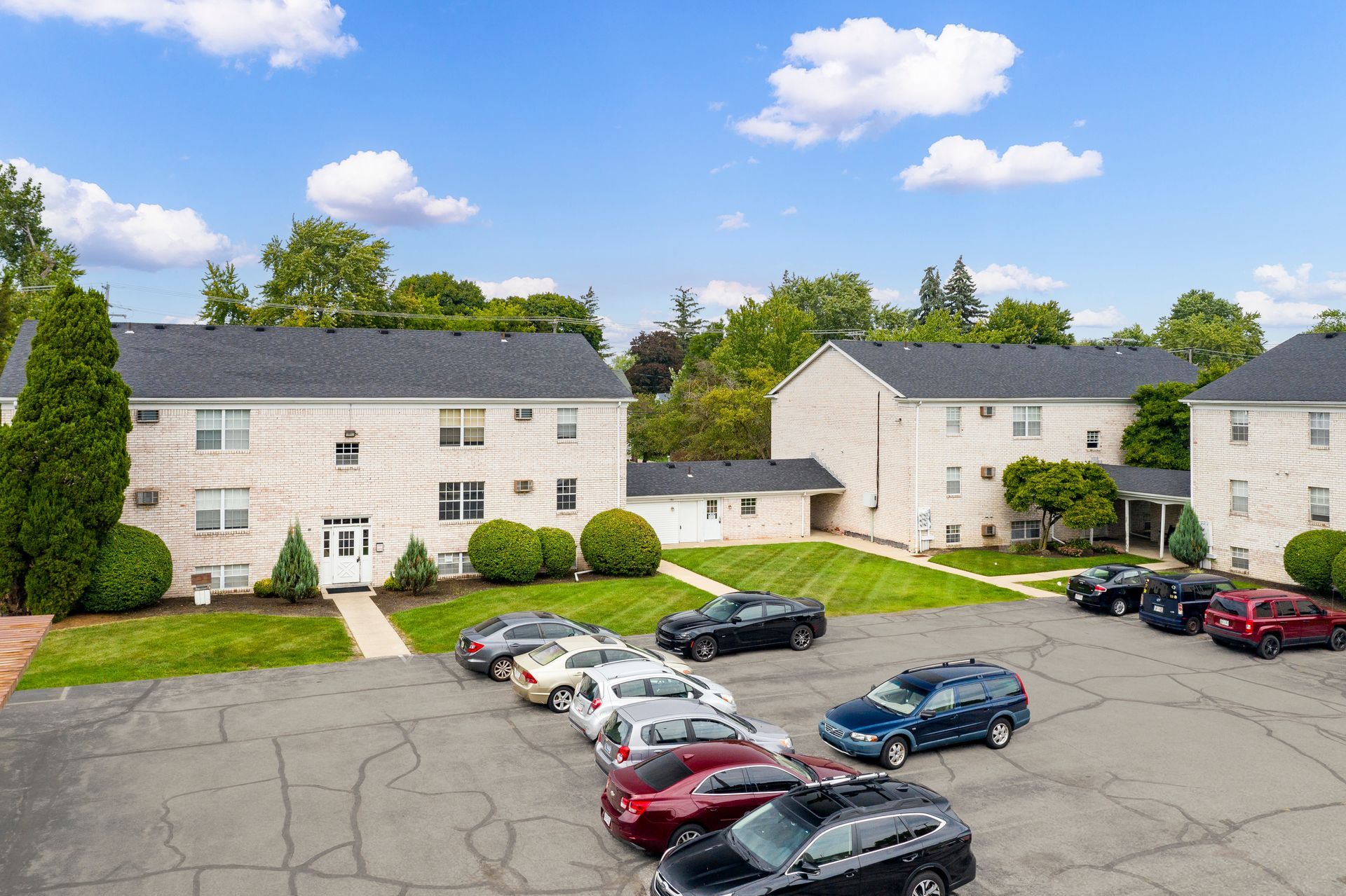 Photo of a community parking lot with three three-story buildings in site and a cloudy sky