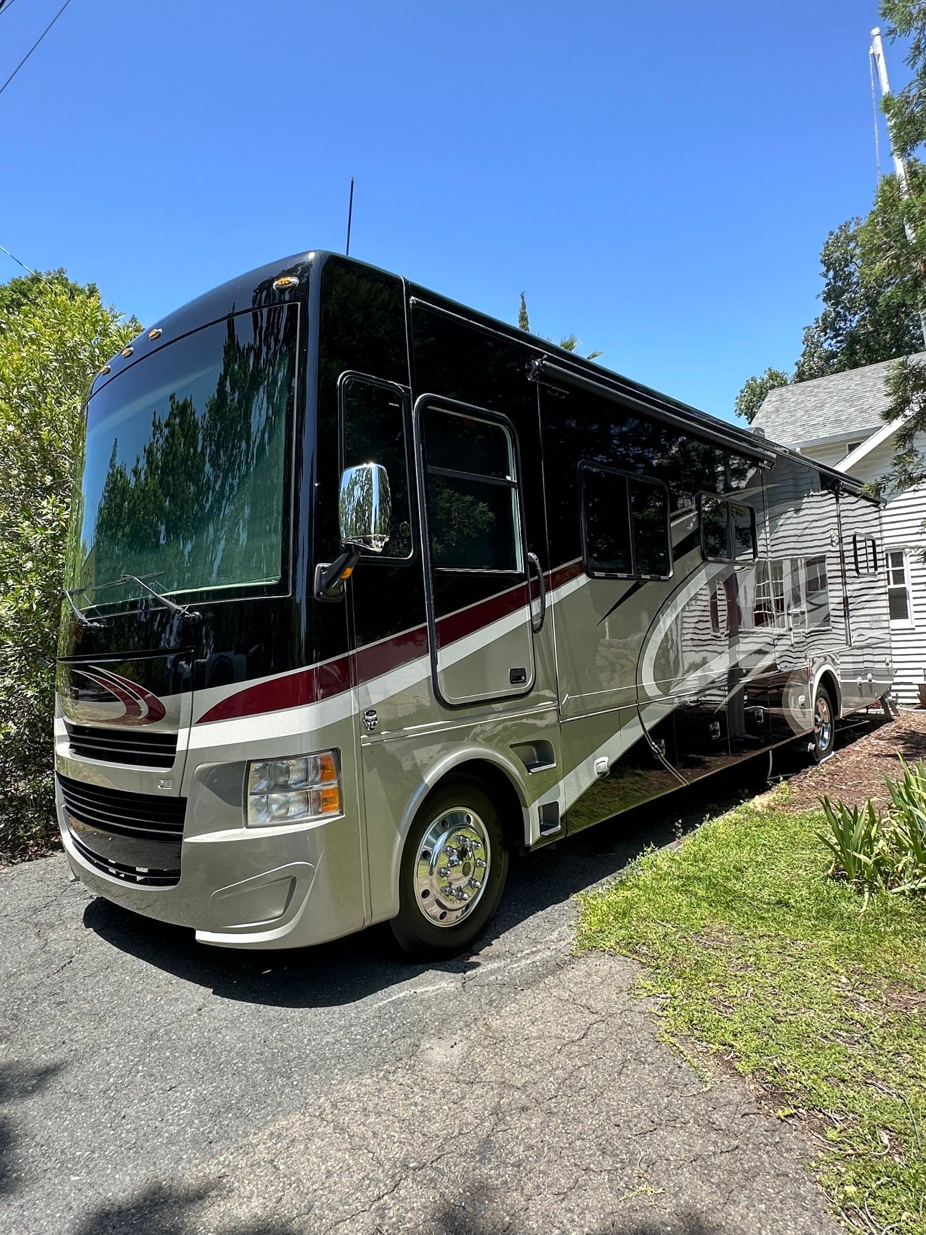 A large rv is parked on the side of a road next to a house.