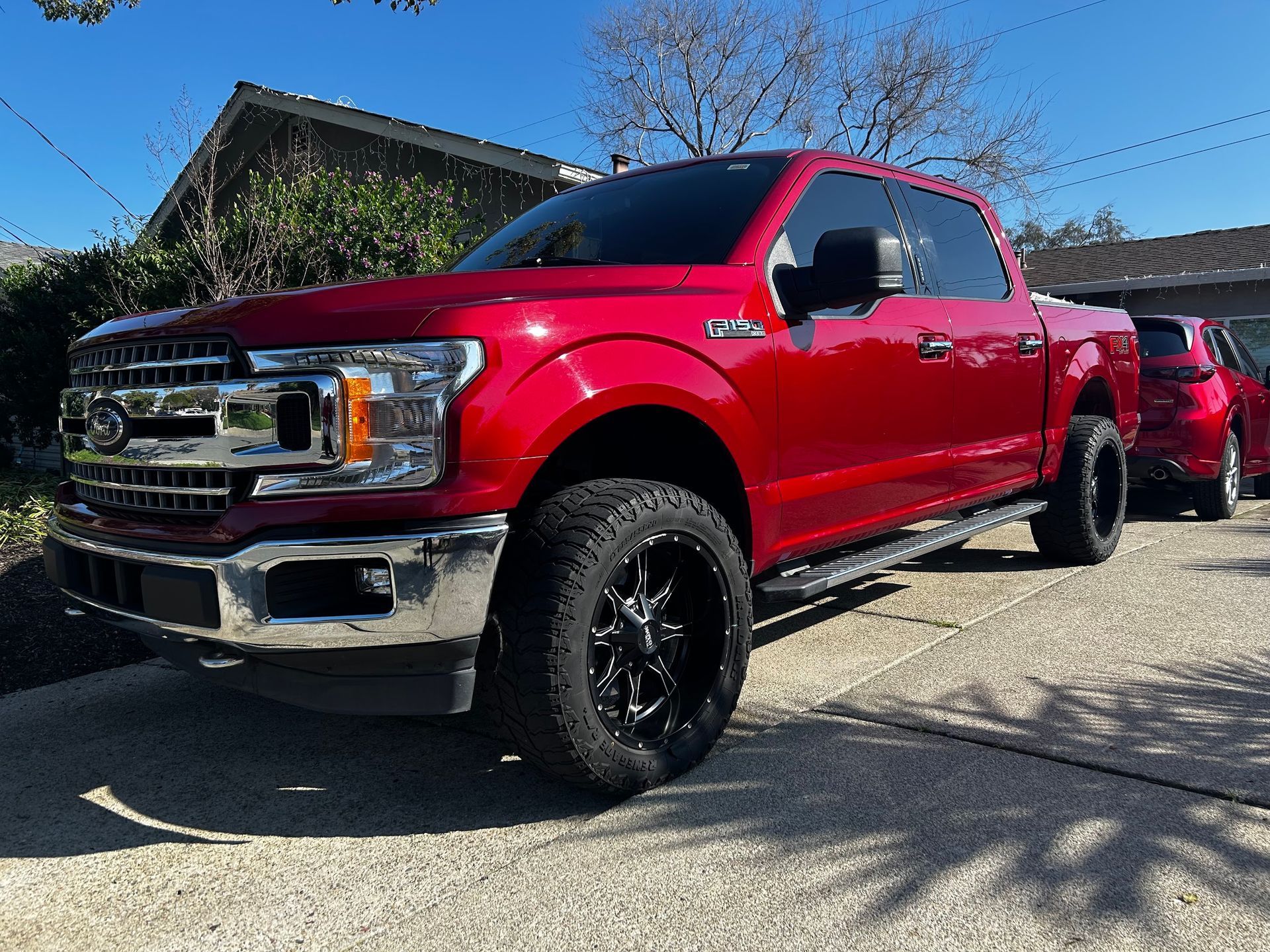 A red ford f150 truck is parked in a driveway in front of a house.