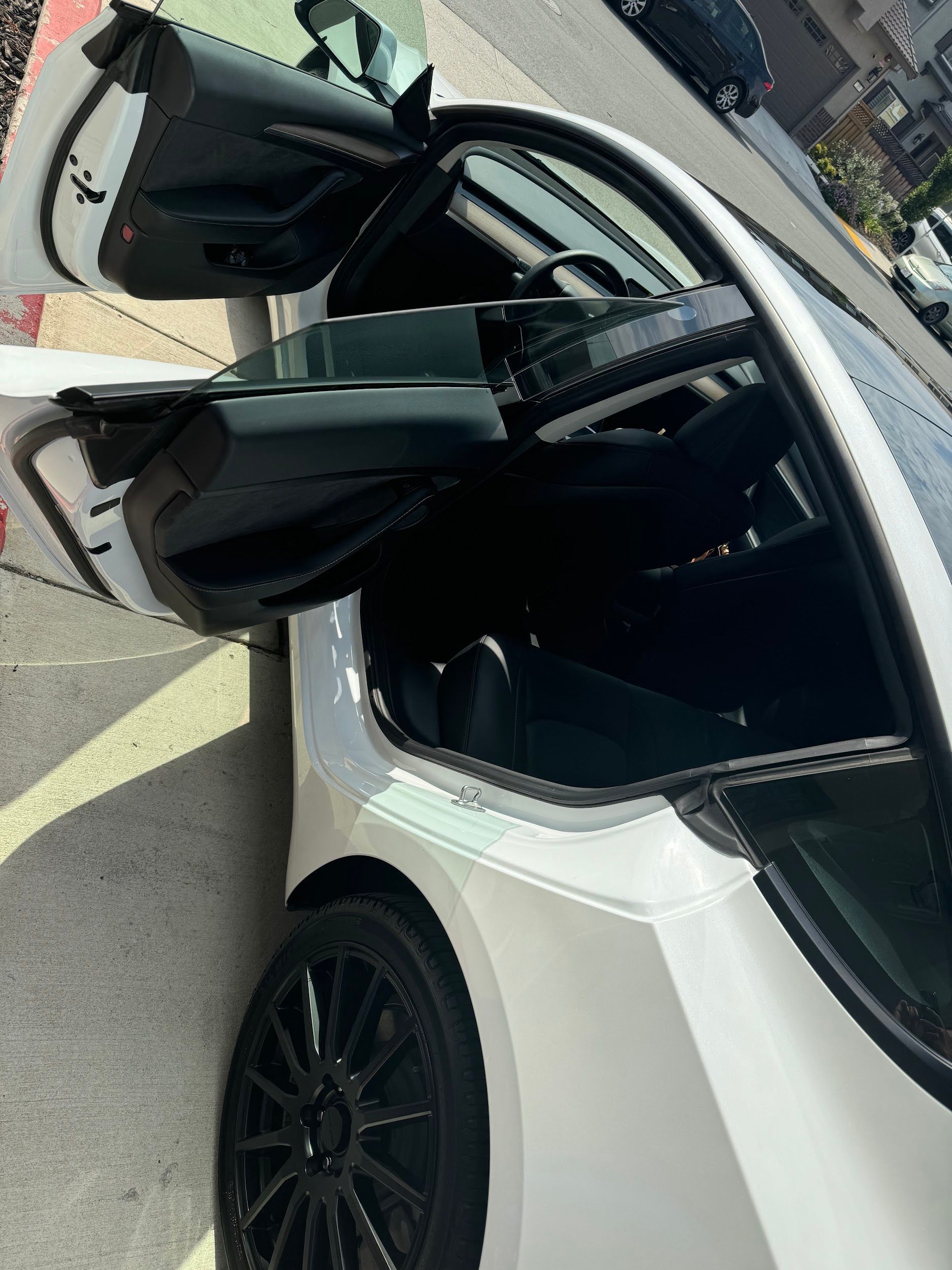 A white sports car with its doors open is parked on the side of the road.