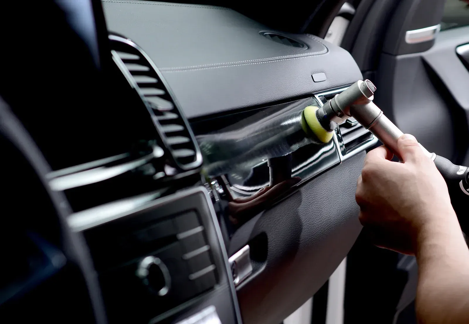 A person is cleaning the dashboard of a car with a brush.