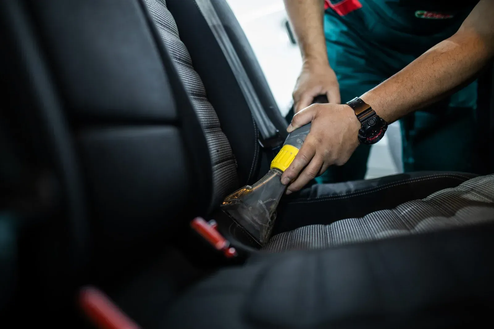 A man is cleaning the seats of a car with a vacuum cleaner.