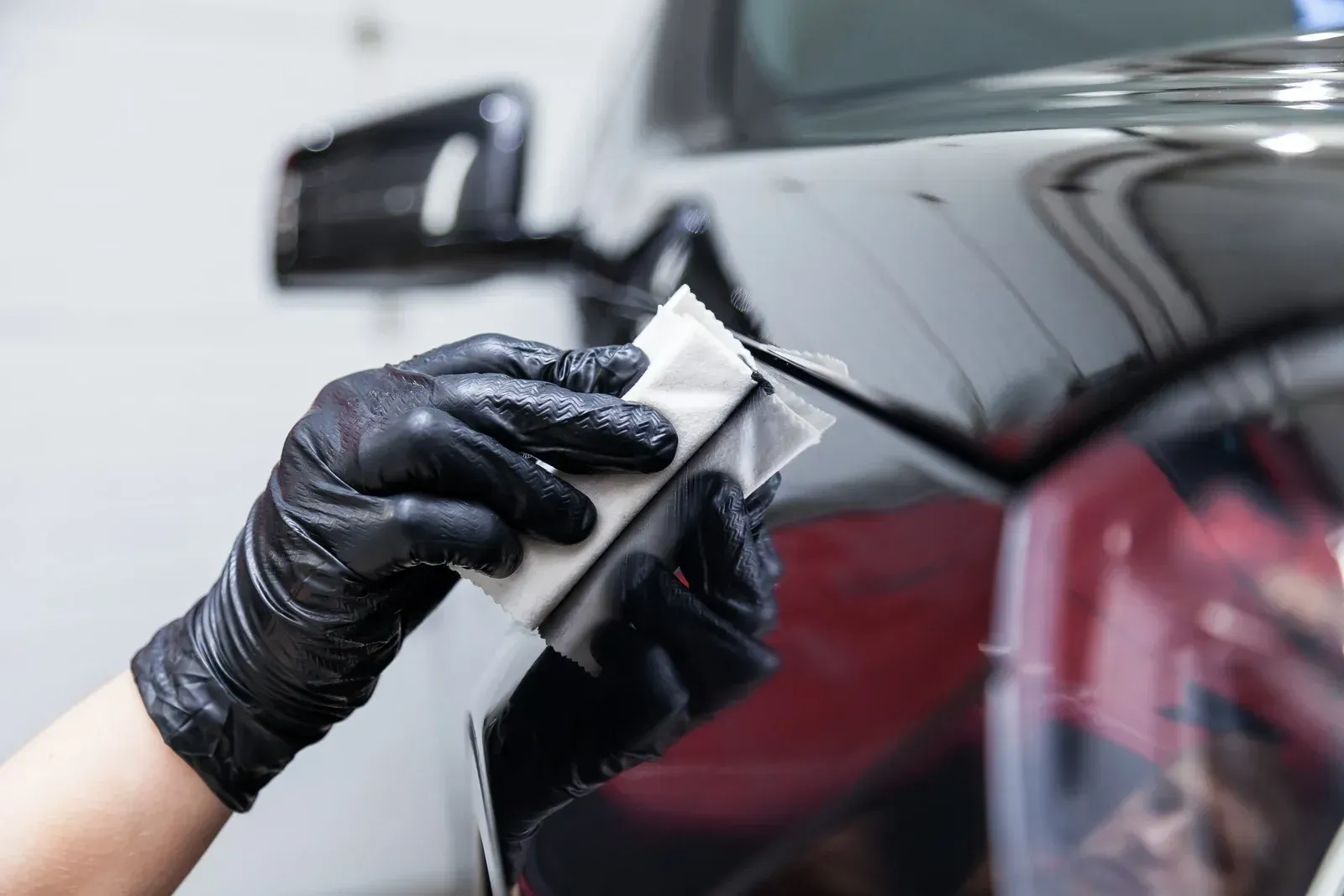 A person wearing black gloves is polishing a black car.