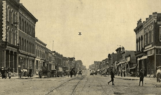 A black and white photo of a city street with horse drawn carriages