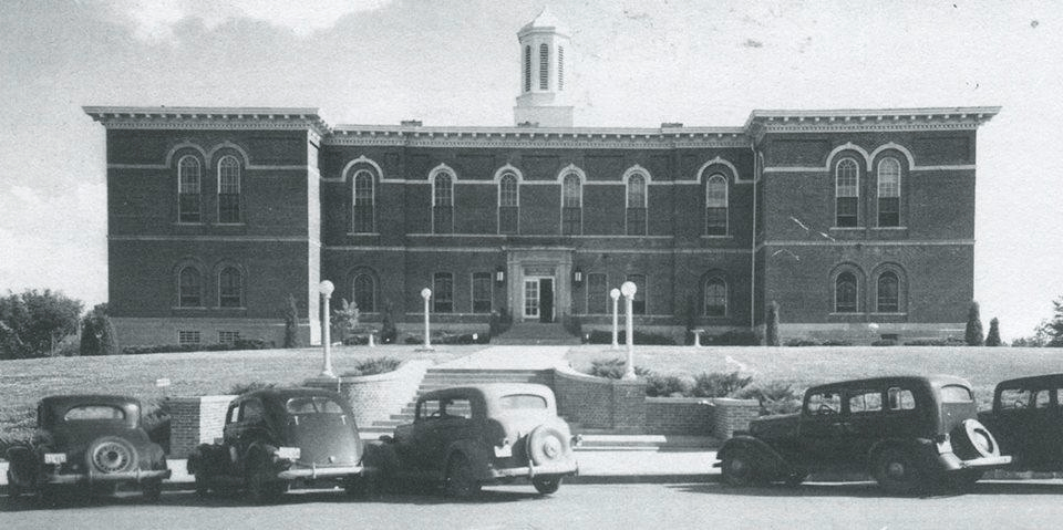 A black and white photo of cars parked in front of a large brick building