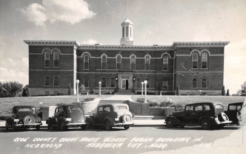 A black and white photo of a large brick building with cars parked in front of it.