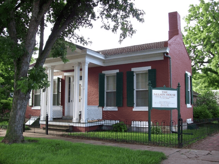 A red brick house with green shutters and a sign in front