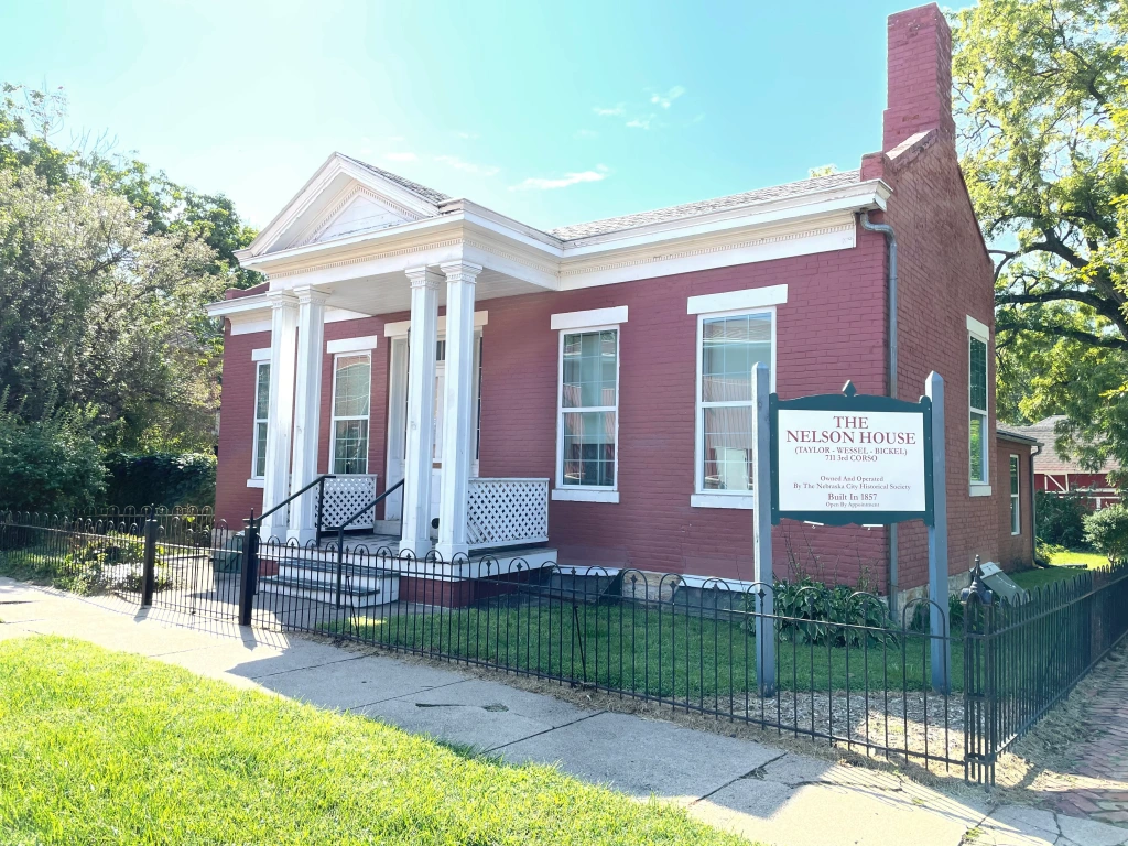 A red brick house with white trim and a sign in front of it. Nelson House.