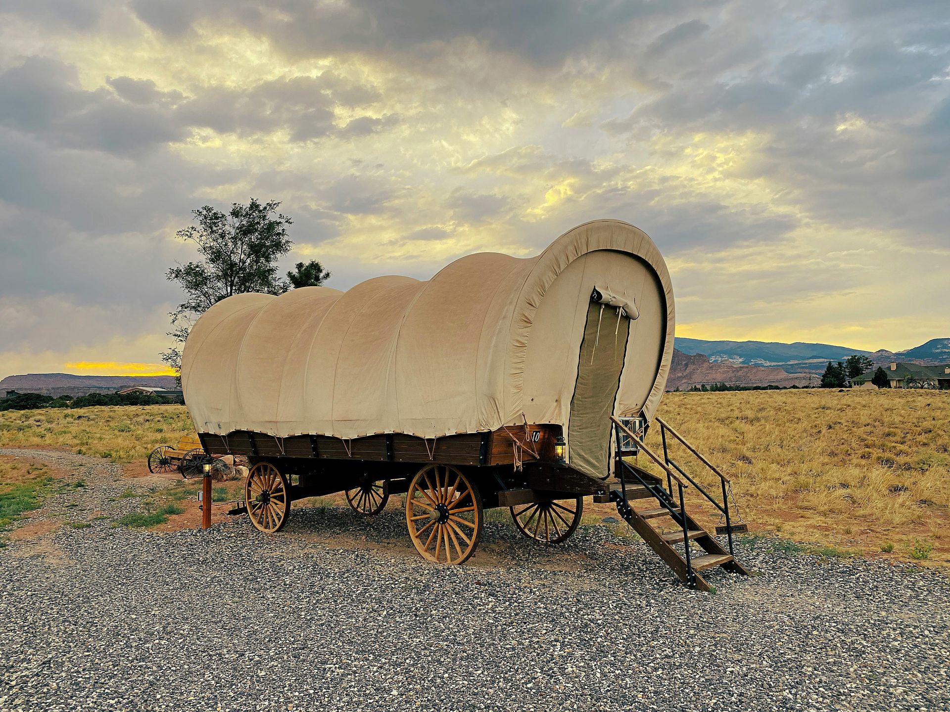 An old covered wagon with stairs is parked in a gravel lot.