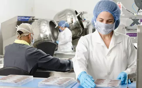 People in lab coats and masks work in a pharmaceutical manufacturing facility.