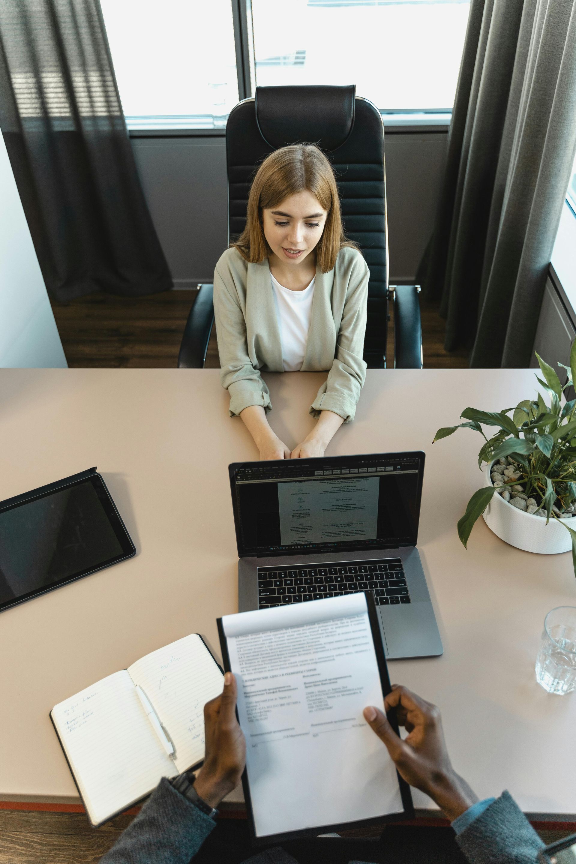Woman in interview seated across from interviewer holding documents at a desk.
