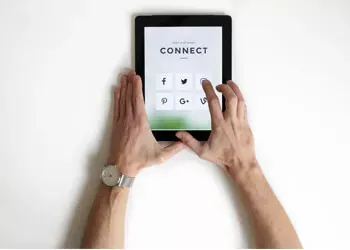 Hands using tablet, showing social media icons, connect screen, on white surface.