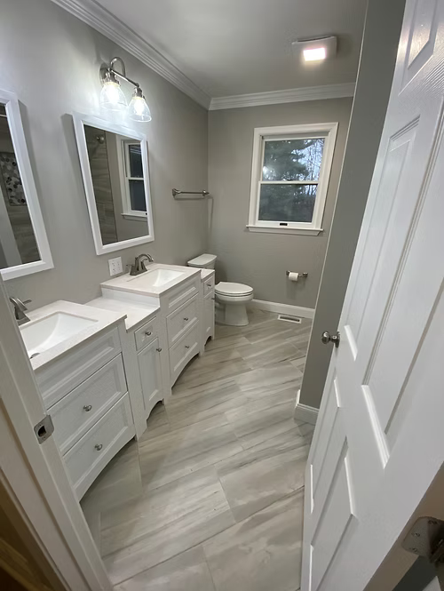 A bathroom with two sinks , a toilet , and a window.
