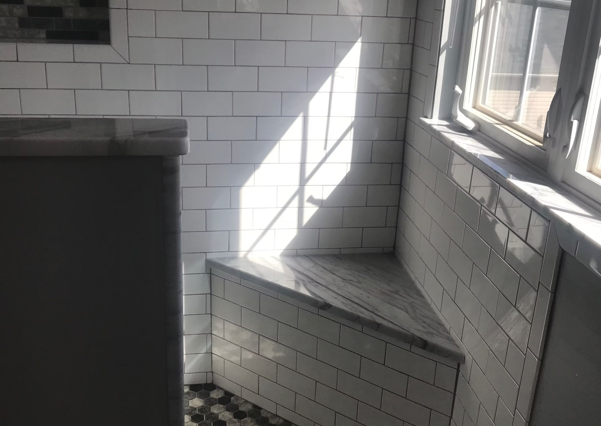 A corner of a room with white tiles and a window.