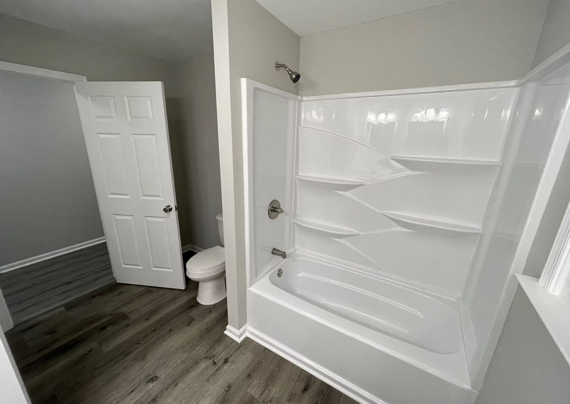 A bathroom with a tub , toilet , shower and shelves.