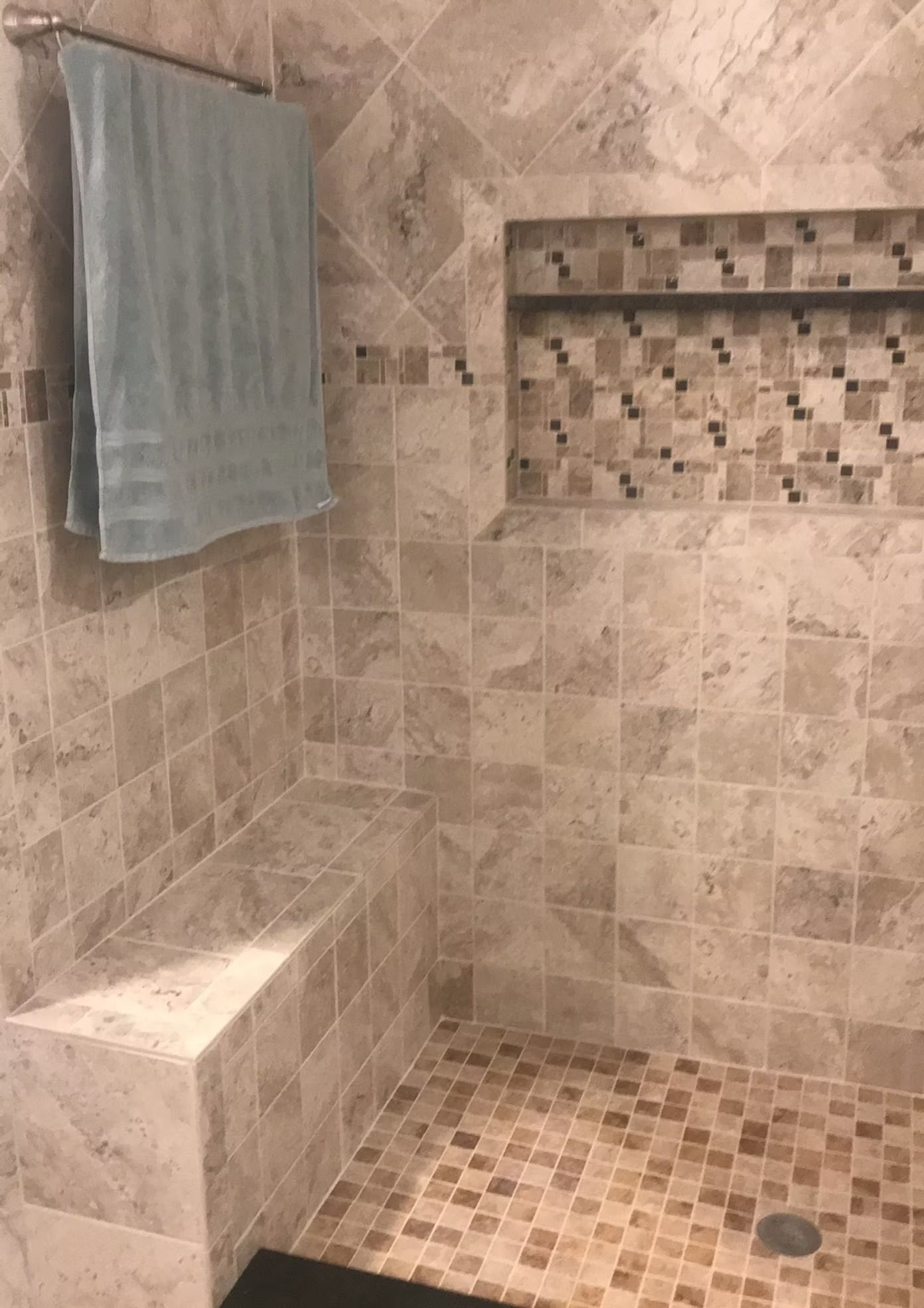 A shower with a bench and a towel hanging on the wall.