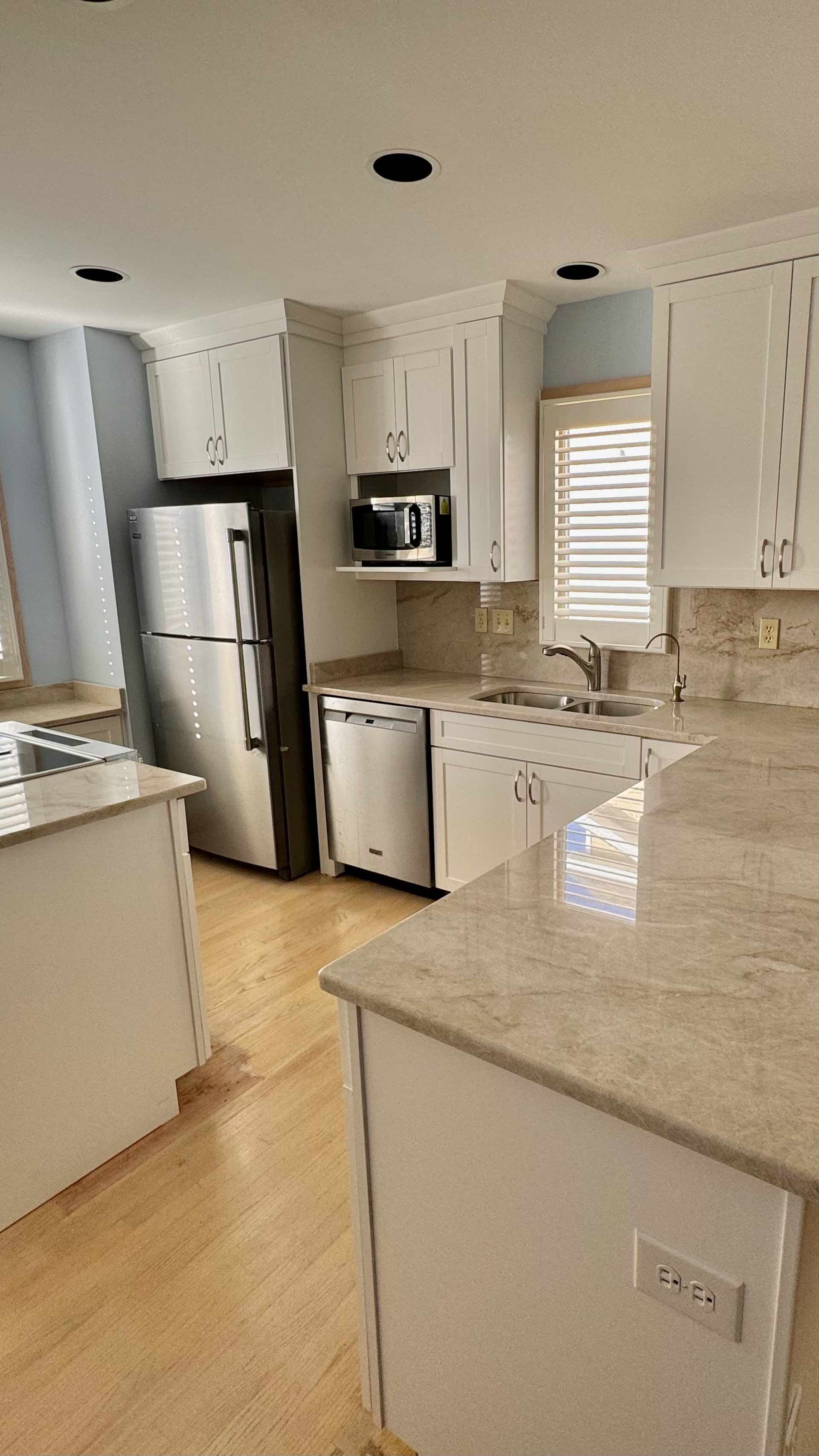 A kitchen with white cabinets , stainless steel appliances , granite counter tops and a refrigerator.