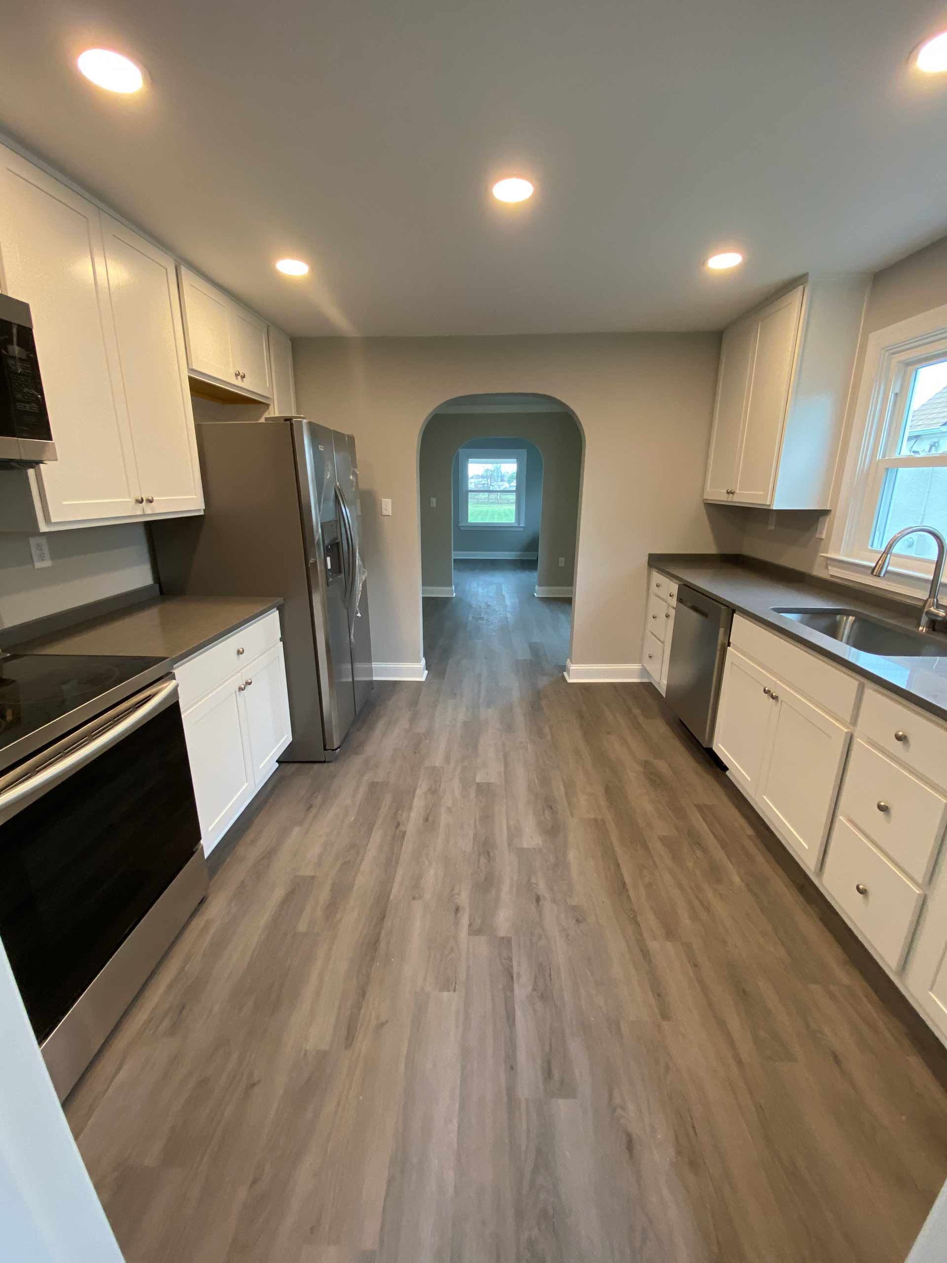 A kitchen with hardwood floors , white cabinets , stainless steel appliances and a refrigerator.