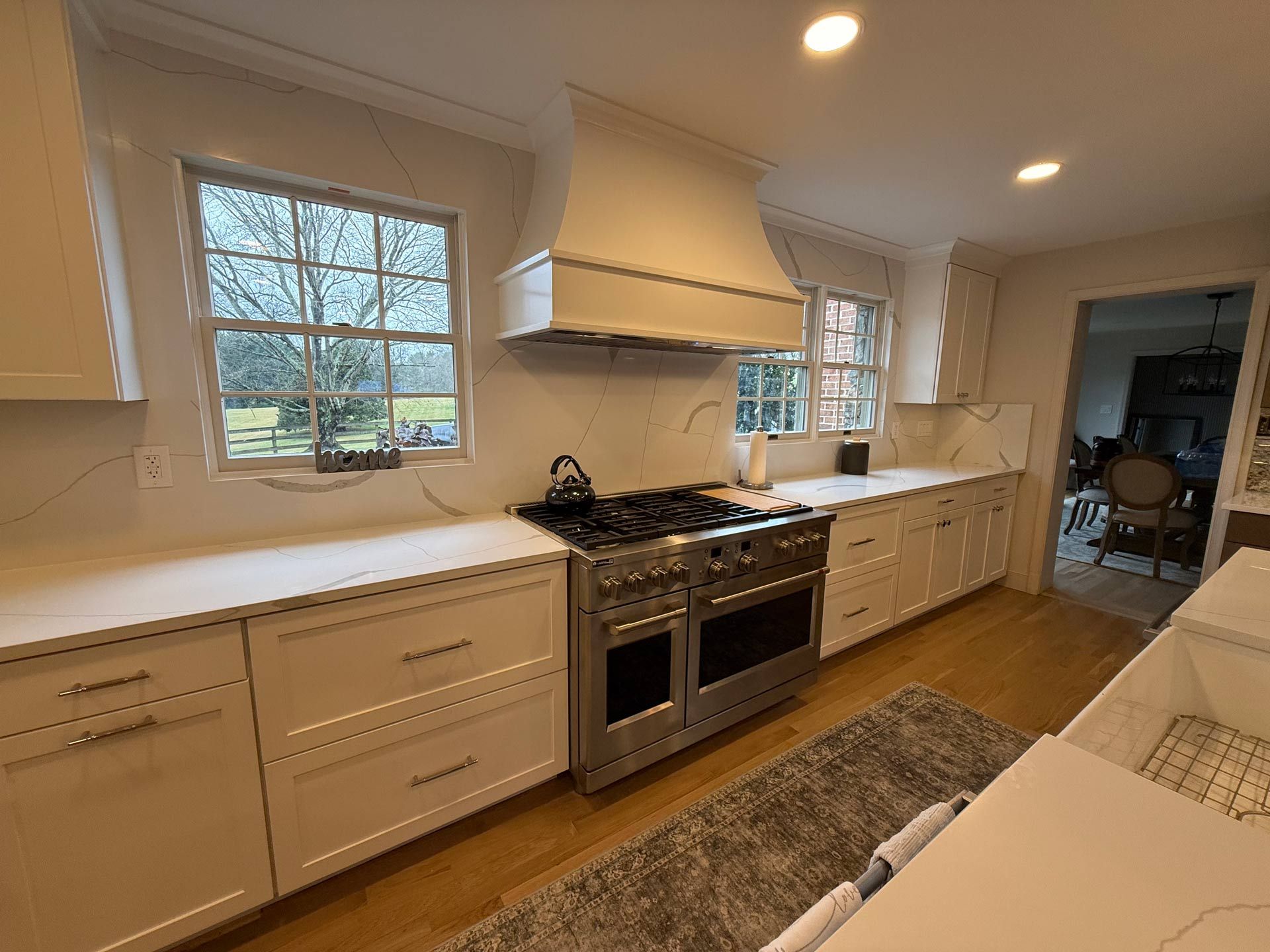 A kitchen with white cabinets , stainless steel appliances , a stove and a window.