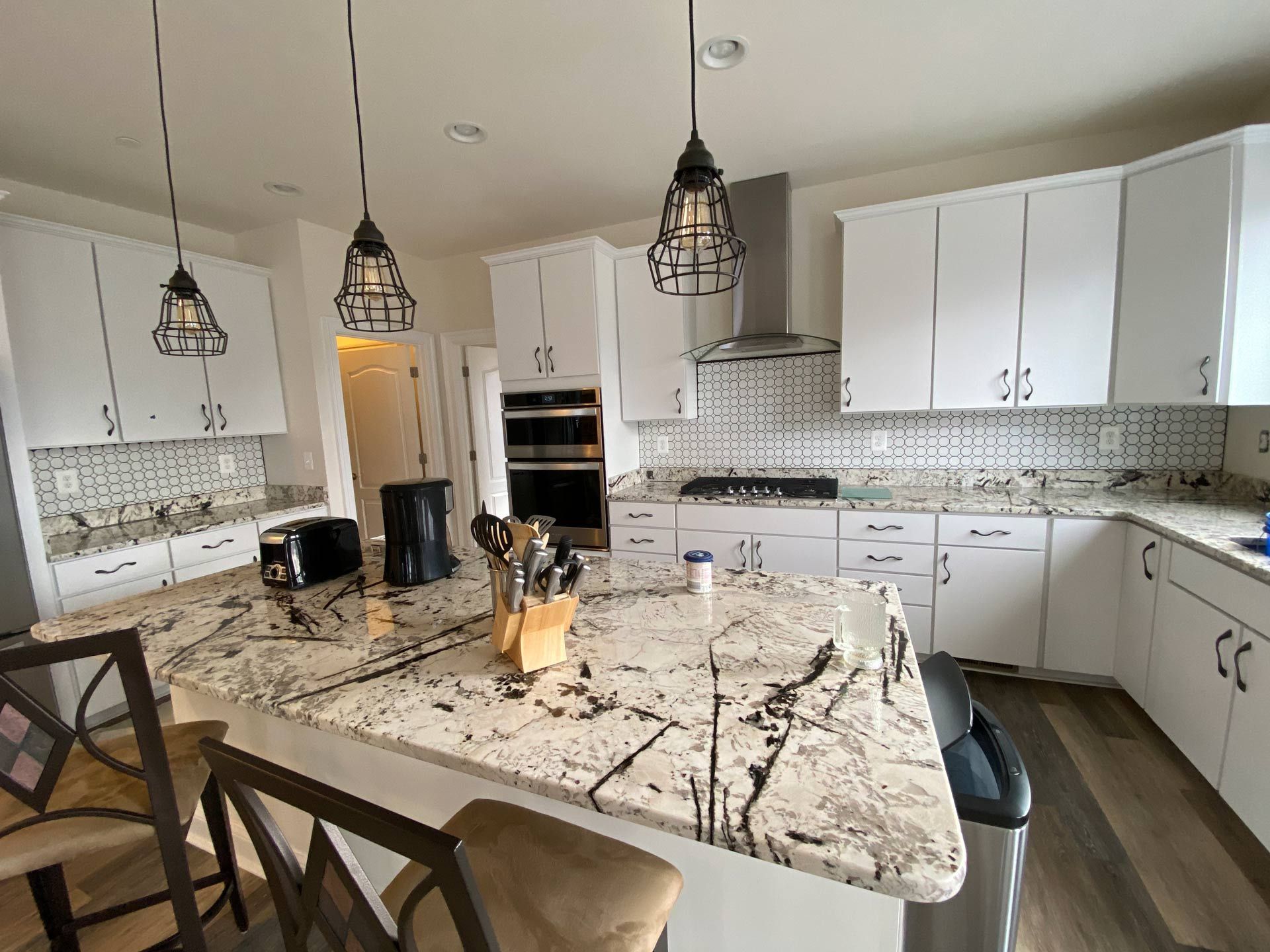 A kitchen with white cabinets , granite counter tops , stainless steel appliances and a large island.