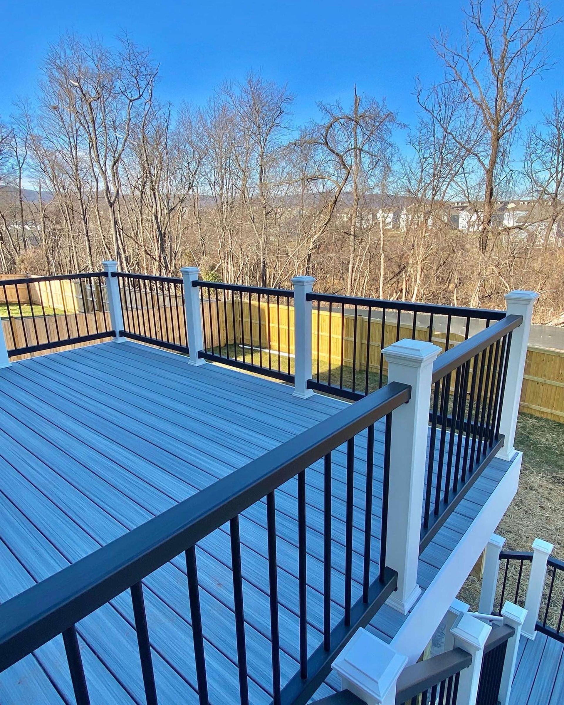 A wooden deck with a black railing and trees in the background.