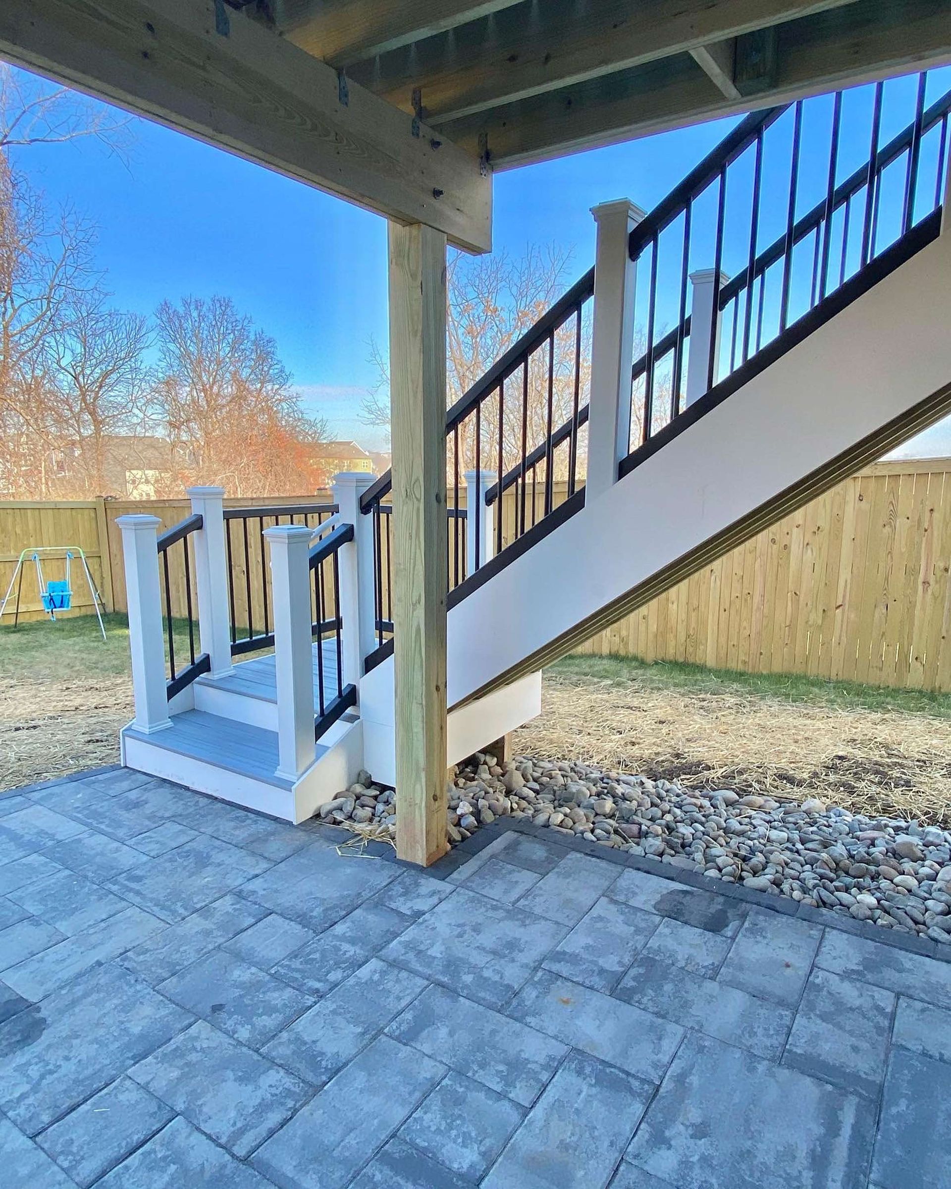 A deck with stairs leading up to it and a wooden fence in the background.